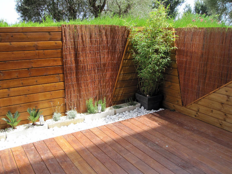 Terrasse en lames de bois bordée de plantations et de canisses