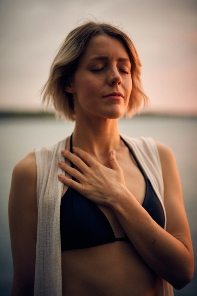 Femme assise en tailleur en pleine méditation au bout d'un ponton au bord d'un lac au lever du soleil pour illustrer la Pratique de la Gratitude, reconnecter à soi, trouver le calme et la sérénité