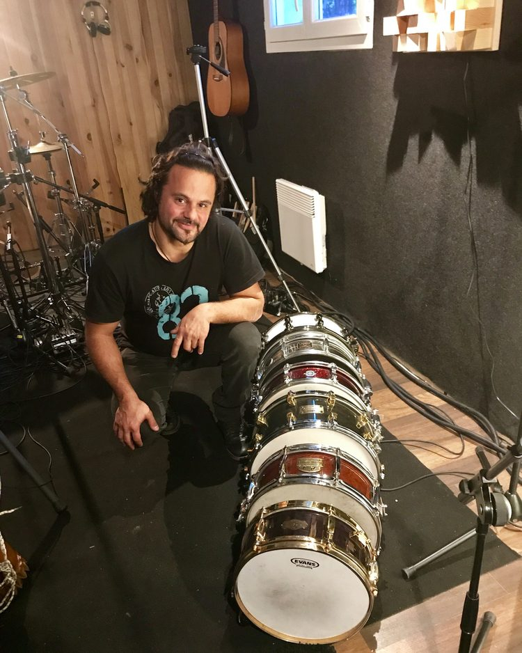 Chris Briand accroupi à côté d'une pile de caisses claires dans son studio